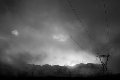 Low angle view of electricity pylon against cloudy sky