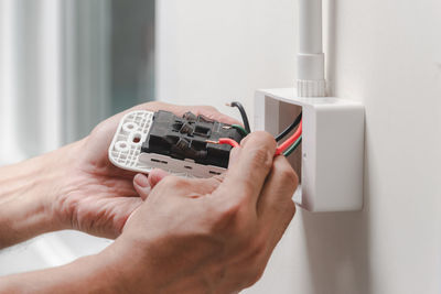 Cropped hands of male electrician repairing electrical outlet on wall