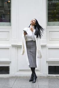 Full length of young woman using phone while standing outdoors