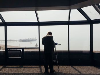 Man standing by window against sky
