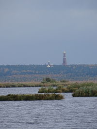 Lighthouse by lake and buildings against clear sky