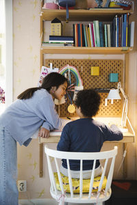 Girl leaning at desk while teaching brother at home