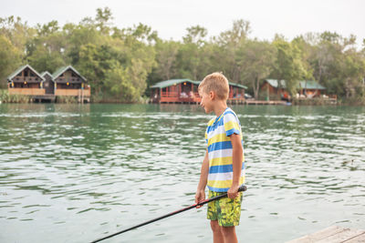 Boy fishing in lake while standing on pier