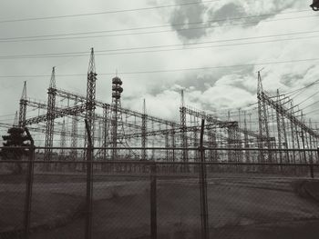 Fence by electricity pylon against sky