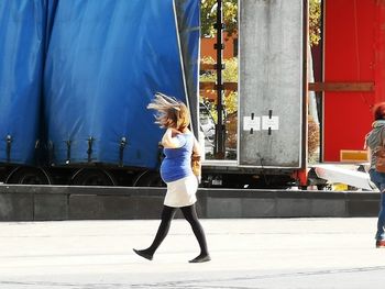 Pregnant woman walking into the wind, crossing a place