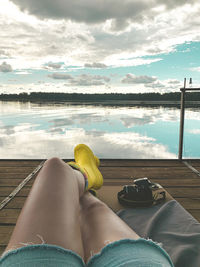 Low section of woman lying on swimming pool against sky