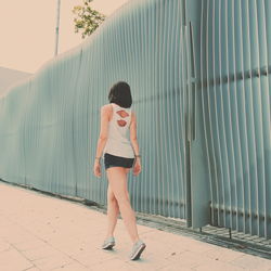 Rear view of mid adult woman walking on footpath against fence