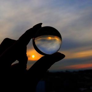 Close-up of silhouette hand holding sun against sky during sunset