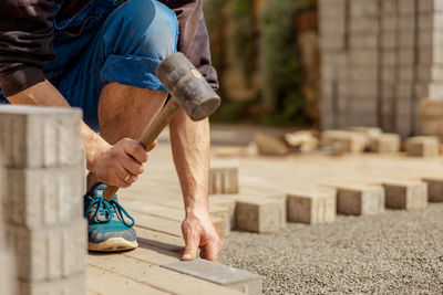 Young man laying gray concrete paving slabs in house courtyard on gravel foundation base. 