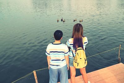 Rear view of friends looking at ducks swimming in lake while standing on pier