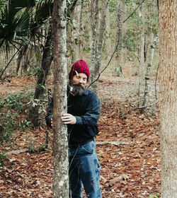 Portrait of woman standing by tree trunk in forest