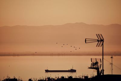 Silhouette birds flying over sea against orange sky