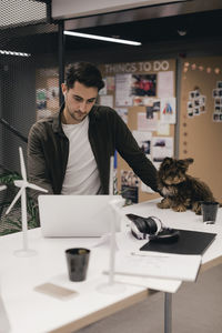 Serious entrepreneur using laptop by dog while working at desk in creative office