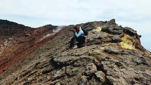 Side view of woman photographing while sitting on volcanic landscape