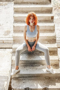 Cheerful woman, relaxing after fitness workout in park, sitting on concrete steps outdoors