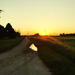 Road amidst field against clear sky during sunset