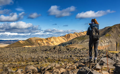 Rear view of man standing on rock against sky