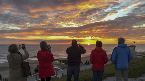 Rear view of people photographing sea against sky during sunset