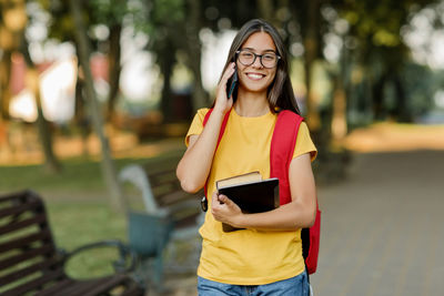 Portrait of a beautiful brunette with glasses and a backpack talking on the phone in the park