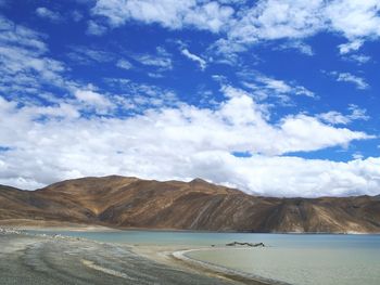 Scenic view of river and mountains against cloudy blue sky on sunny day