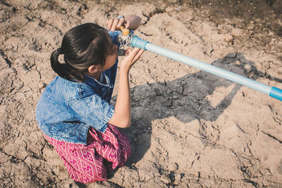 High angle view of girl crouching by faucet during drought