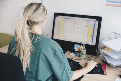 Rear view of female nurse working at computer in doctor's office