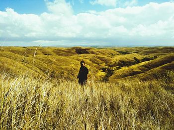 Man standing on landscape against cloudy sky