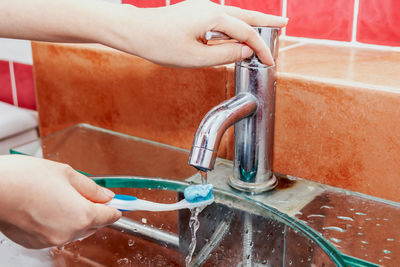 Midsection of person putting toothbrush under water tap