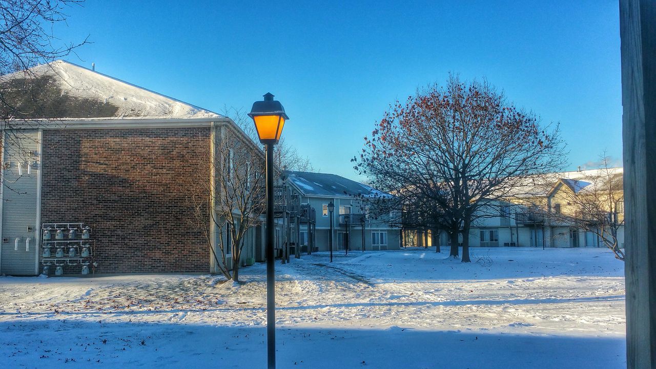 clear sky, built structure, building exterior, blue, architecture, street light, tree, snow, sunlight, bare tree, winter, railing, sky, lighting equipment, outdoors, day, street, city, cold temperature, shadow