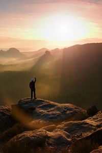 Man takes photos with smart phone on peak of rock empire. dreamy fogy landscape, spring orange mist