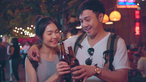 Smiling young couple toasting beer bottles at night