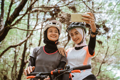 Smiling young females taking selfie against trees