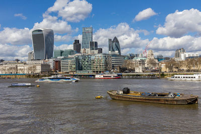 Boats in river by buildings in city against sky