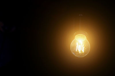 Low angle view of illuminated light bulb in darkroom