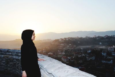 Woman wearing hijab standing by retaining wall against sky