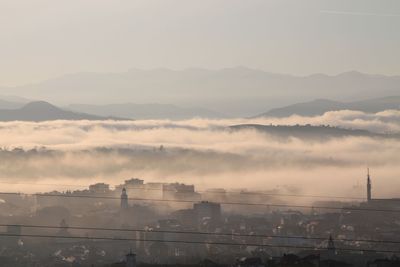 Aerial view of cityscape in foggy weather against sky during sunset