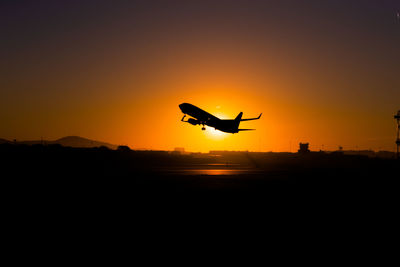 Silhouette airplane flying against orange sky