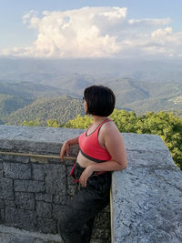 Rear view of woman sitting on retaining wall against mountain