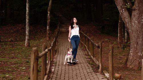 Full length of young woman and dog on skateboard in park