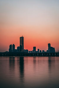 Scenic view of lake by buildings against sky during sunset