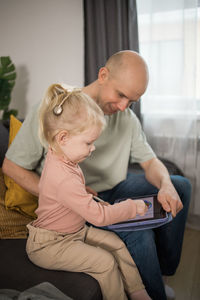 Mother and daughter using digital tablet while sitting on sofa at home