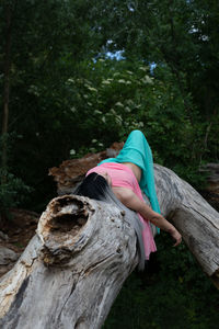 Rear view of woman sitting on tree trunk in forest