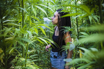 Young woman smoking cigarette while standing amidst plants