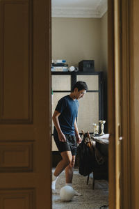 Teenage boy playing with soccer ball in bedroom at home