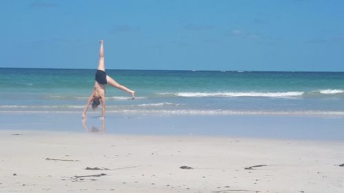 Full length of woman doing handstand on shore at beach against sky