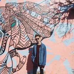 Young man standing against graffiti wall on sunny day