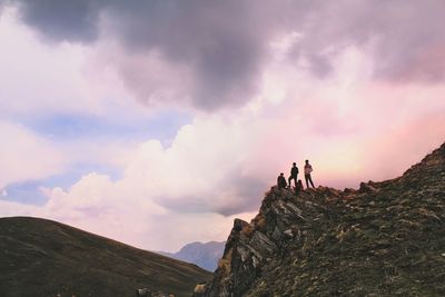 Low angle view of hikers standing on cliff against cloudy sky