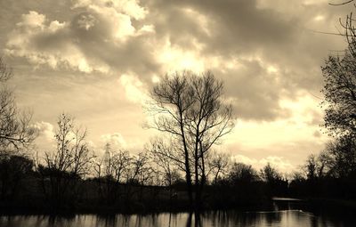 Silhouette bare trees by lake against sky during sunset