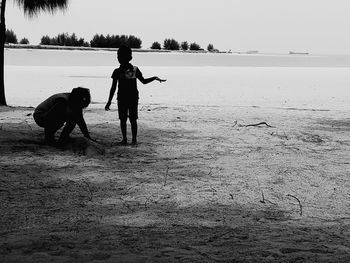 Children playing on sand at beach against sky