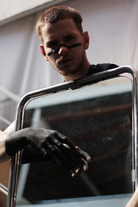 Portrait of young man with face paint holding mirror standing outdoors